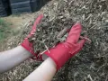 Ręce w czerwonych rękawiczkach trzymają garść materiału, który posłuży jako mulcz.
