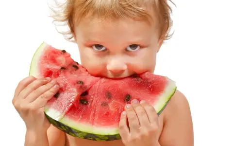 Małe dziecko z apetytem wgryza się w soczystego arbuza. Może to inspiracja, jak zasadzić arbuza z pestki i doczekać się własnych owoców.