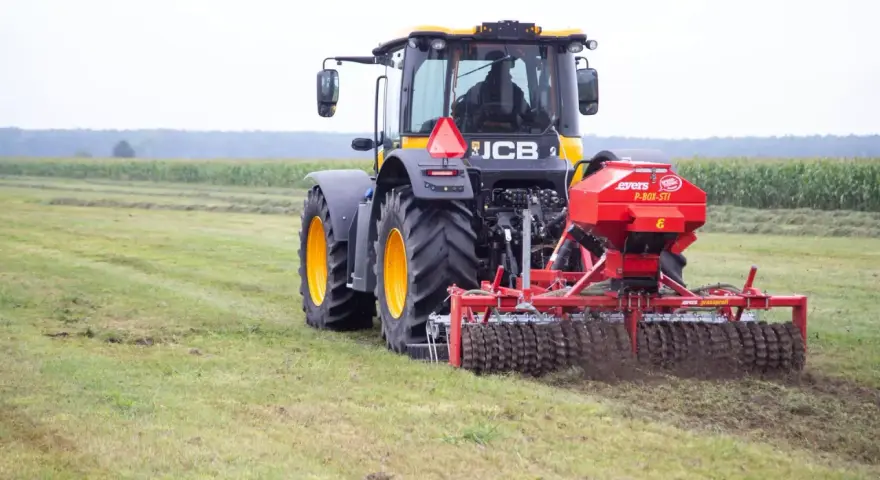 Ciągnik JCB z rozsiewaczem nawozu na polu.